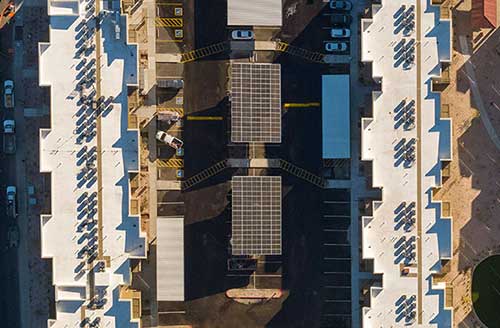 Modern apartment complex with solar panels and parking lot in an aerial view.